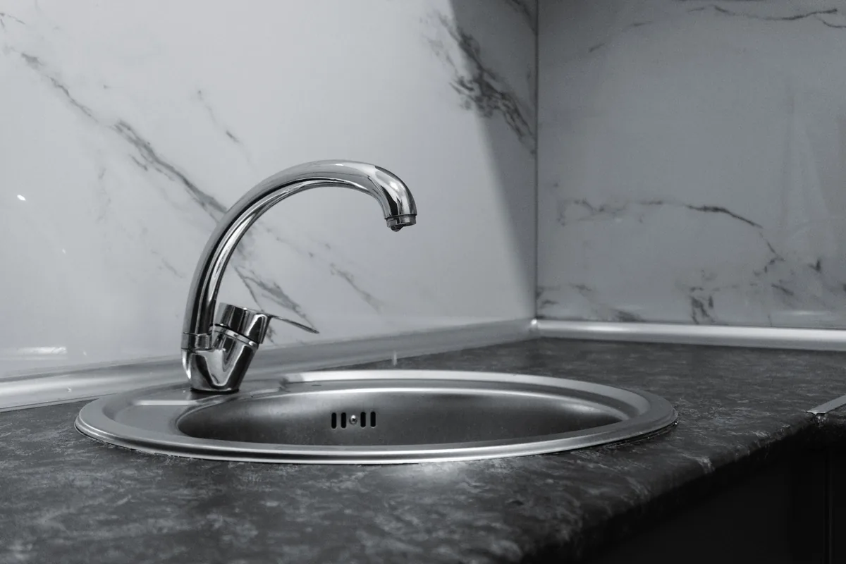 Under-mount stainless kitchen sink sealed to the underside of a quartz countertop with braided supply lines and a P-trap below